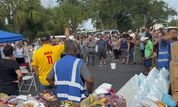 Voluntarios de diversas nacionalidades clasificando cajas de agua embotellada y alimentos no perecederos en un centro de recolección de Florida.