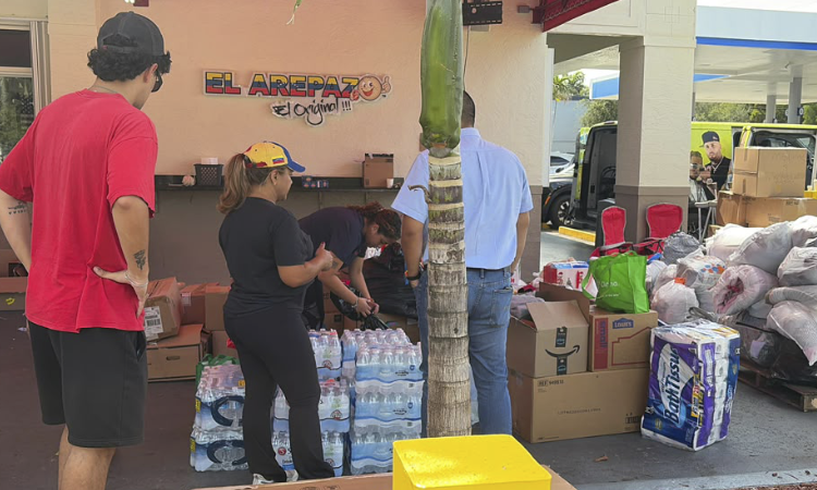 Voluntarios de diversas nacionalidades clasificando cajas de agua embotellada y alimentos no perecederos en un centro de recolección de Florida.2